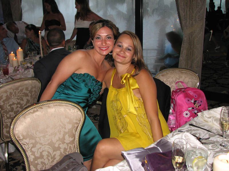 Two women smiling at a table, one in green dress, the other in yellow.
