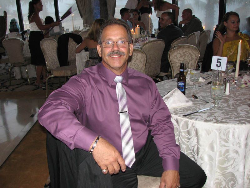 Man in purple shirt and striped tie, smiling, seated at a table in a banquet hall.