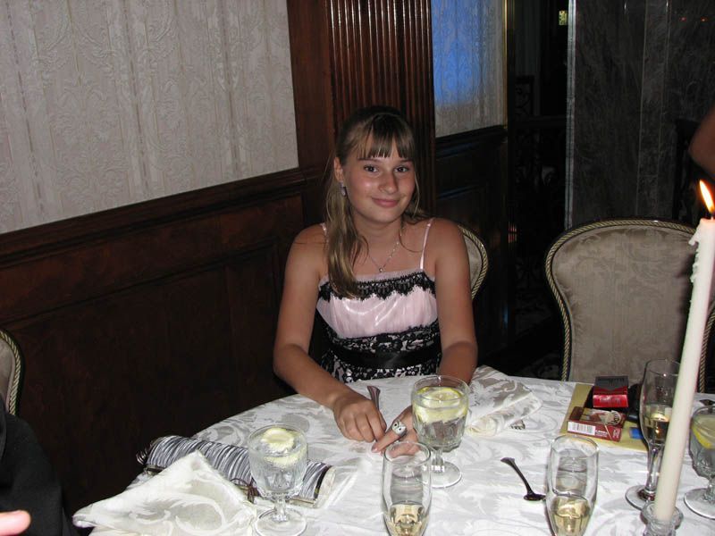Young person seated at a table, wearing a pink and black dress. Lit candles and glasses on the table.