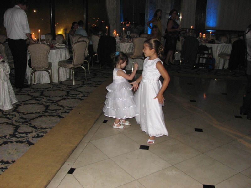 Two young girls in white dresses dancing at a wedding reception.