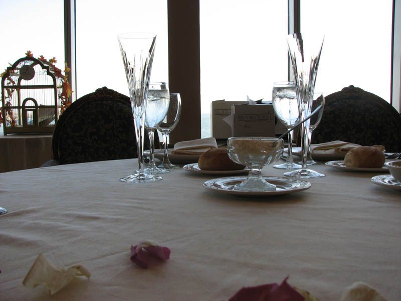 Table setting with crystal glasses, water glasses, plates, and rolls, in front of a window.