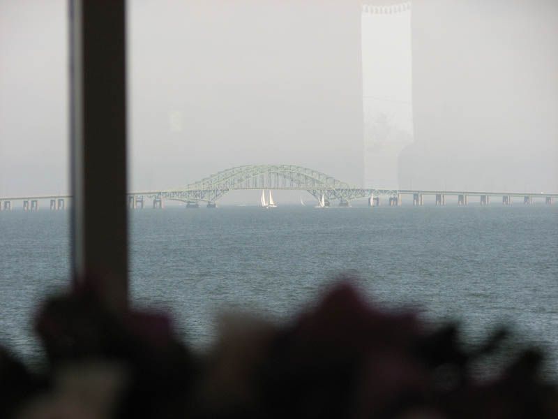 Bridge over water, view through a window, with sailboats in the distance.