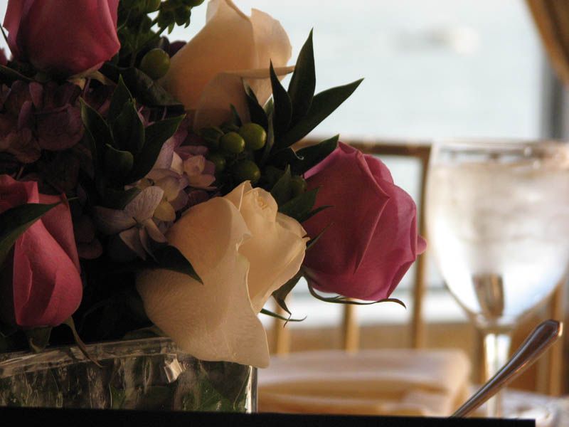 Close-up of a floral arrangement with pink and white roses near a water glass and table setting.