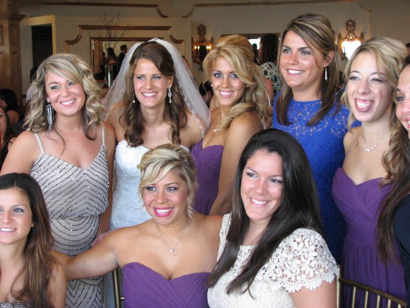 Bridesmaids and bride pose, some in purple dresses, smiling in a well-lit indoor setting.