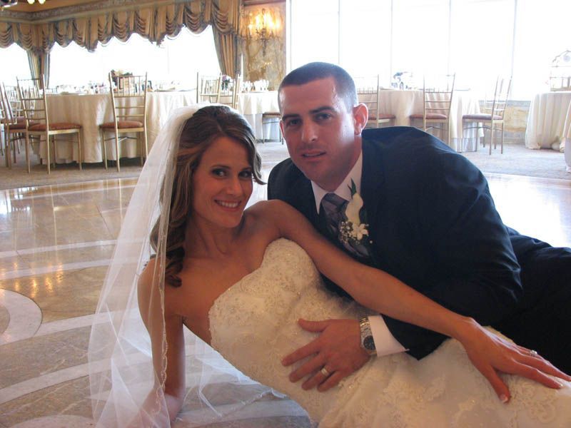 Bride and groom on ballroom floor, bride in white dress, groom in suit, both smiling.