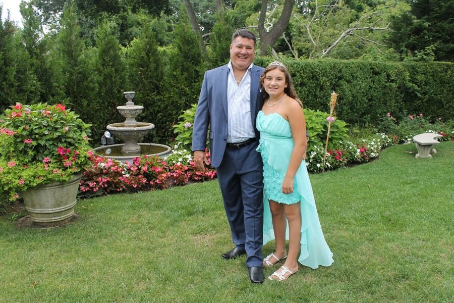 Man and girl posing outdoors near fountain; man in blue suit, girl in turquoise dress.