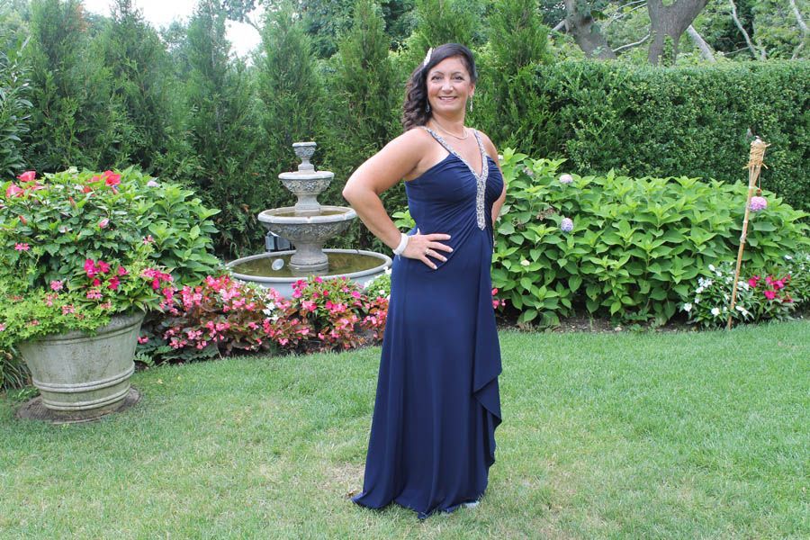 Woman in blue formal gown, posed in garden with fountain and greenery.