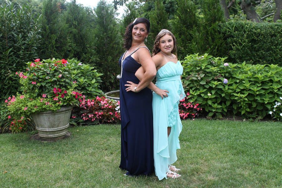 Two people in formal dresses stand back-to-back in a garden.