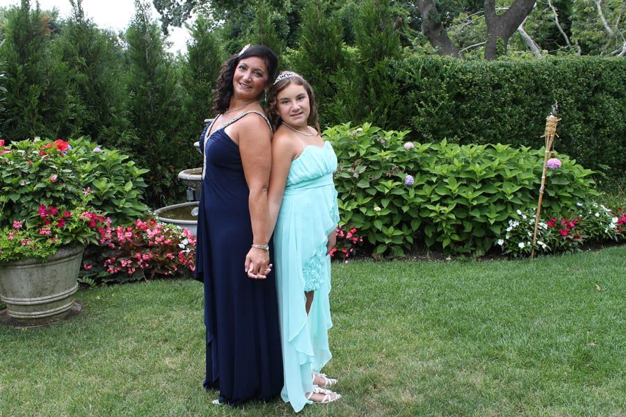 Two people in formal dresses holding hands, standing in a garden.