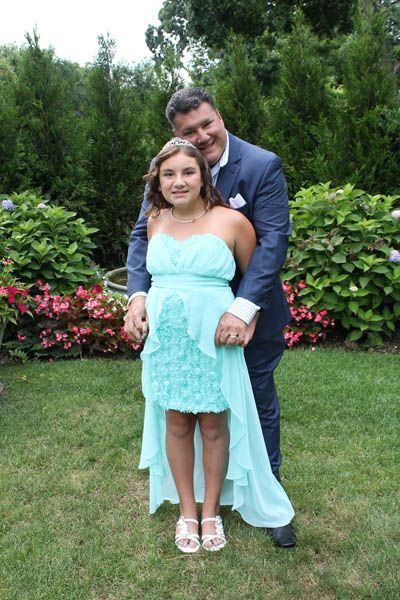 Man hugs girl in a mint dress, both smiling, outdoors with greenery.