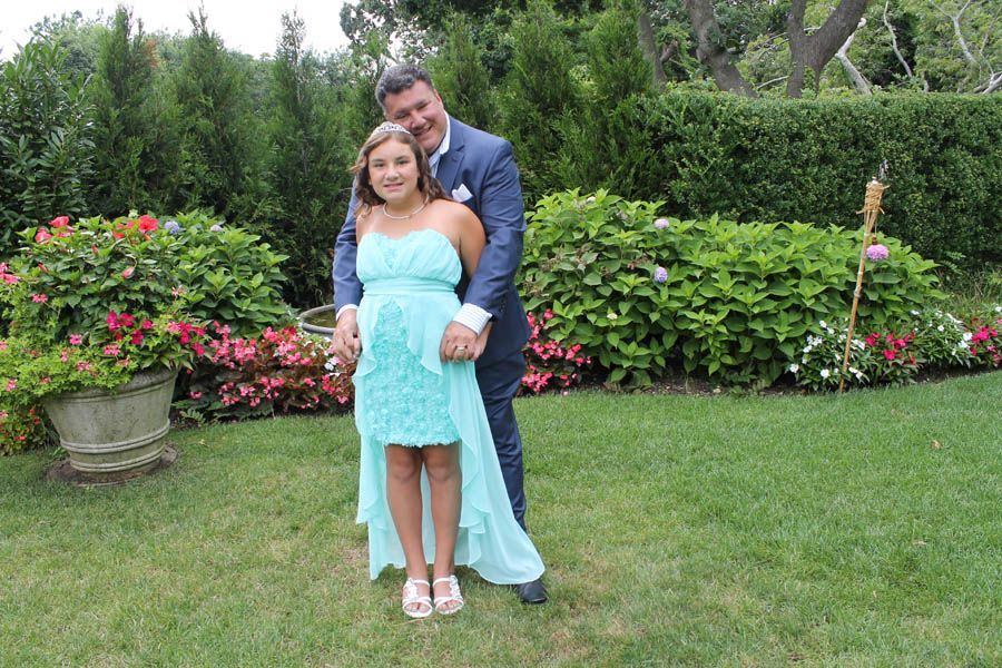 Man and girl pose in a garden. Man in a suit embraces girl in a blue dress.