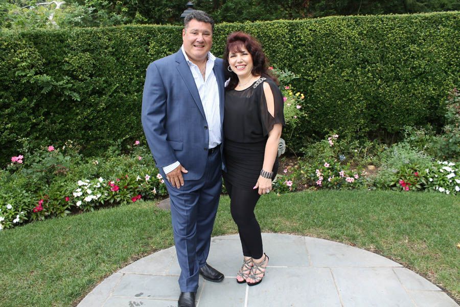 Man in suit and woman in black dress standing outside, smiling.