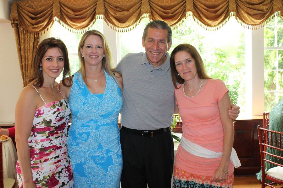 Four people smiling and posing indoors near a window. Two women flank a man. The third woman stands to the right.