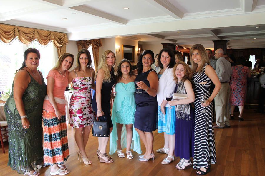 Group of women posing together indoors; various dresses, smiles, and light wood flooring.