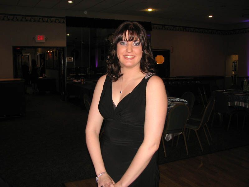 Woman in a black dress smiles at the camera in a dimly lit banquet hall.