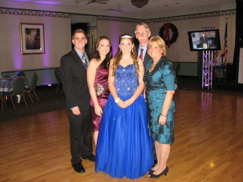 Family of five dressed formally posing on a dance floor. A woman in a blue gown stands center.