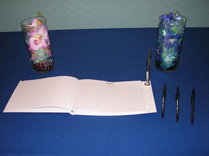 Guest book setup with pens, decorated vases, on a blue tablecloth.