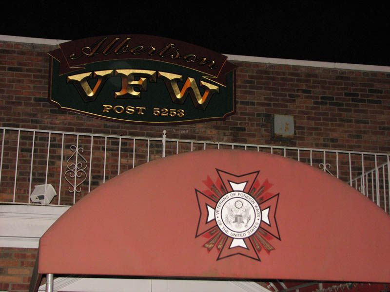 Sign for American VFW Post 5253, with a canopy featuring a red and white emblem. Brick wall background.