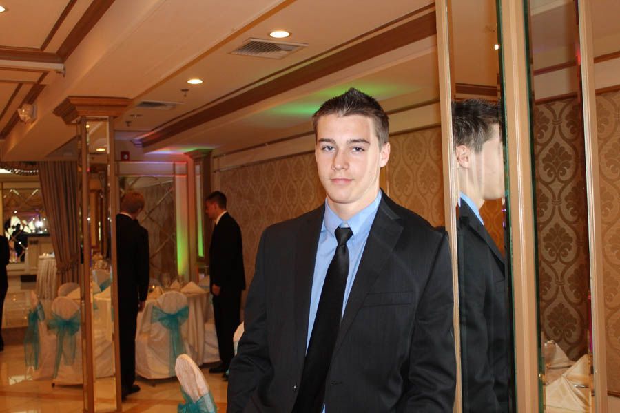 Man in suit leans against a mirror in a decorated event space.
