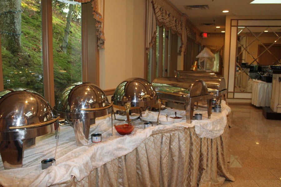 Buffet table with silver chafing dishes and food containers set up for an event, near a window.