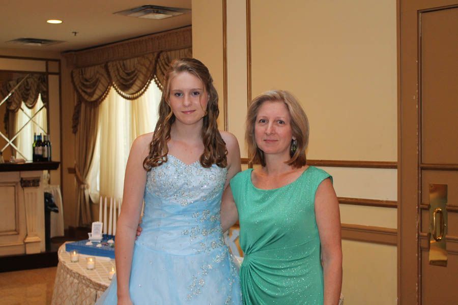 Woman in green dress and young person in blue dress pose indoors, next to a table with candles.