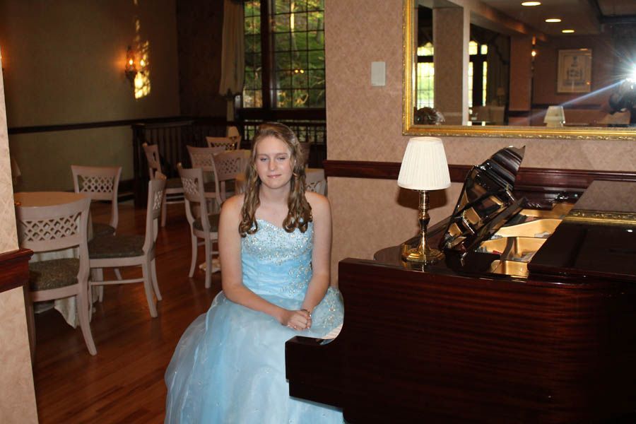 Woman in a blue dress sits at a grand piano in a dining room.