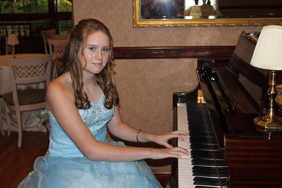 Young person in blue formal dress playing a piano in a restaurant setting.