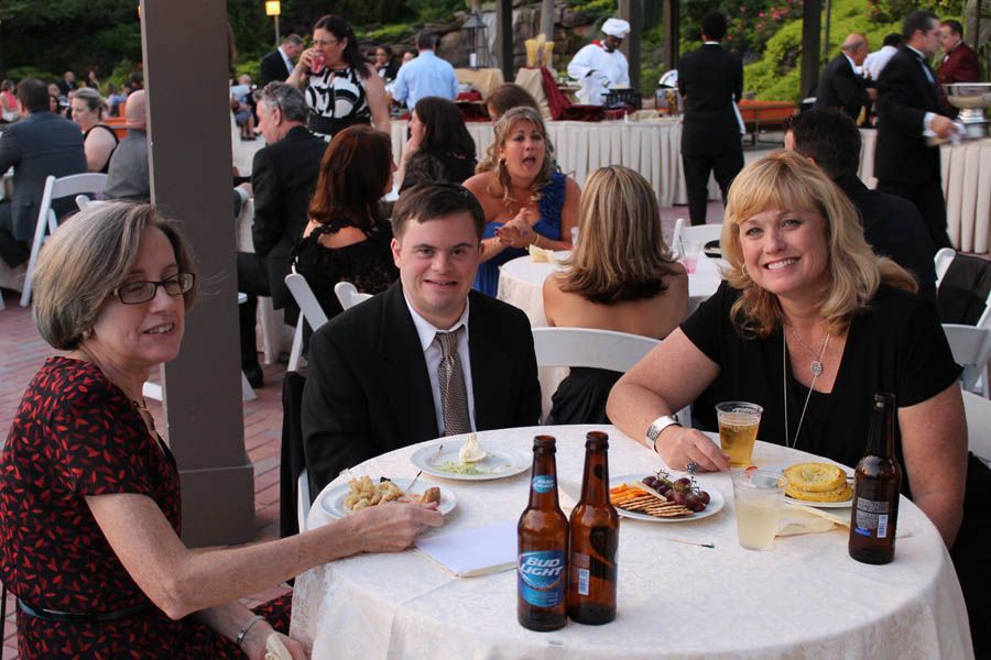 Three people seated at a table at an outdoor event, eating and drinking. Two beer bottles visible.