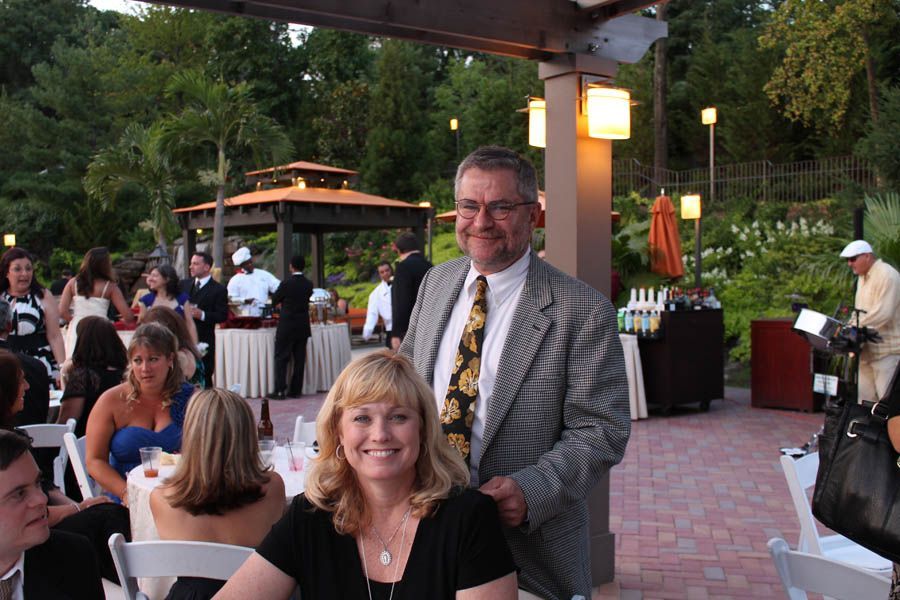 Couple smiling at a formal outdoor event. Background features a gazebo, tables, and people.