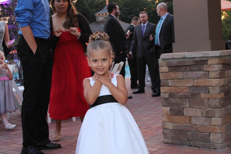 Girl in white dress with hands clasped, smiling at camera at outdoor event.