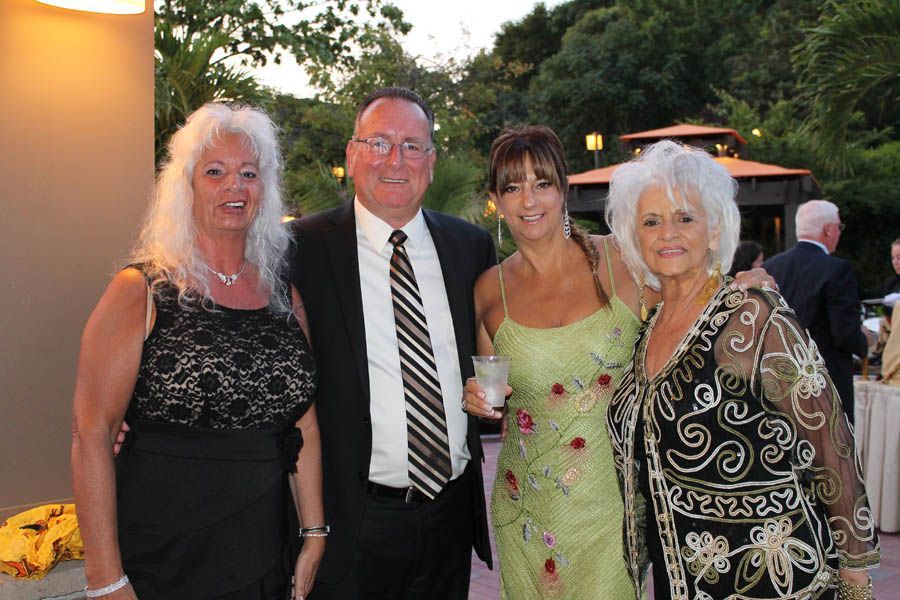 Four people, two women and a man, pose outside; woman in green dress holding drink.