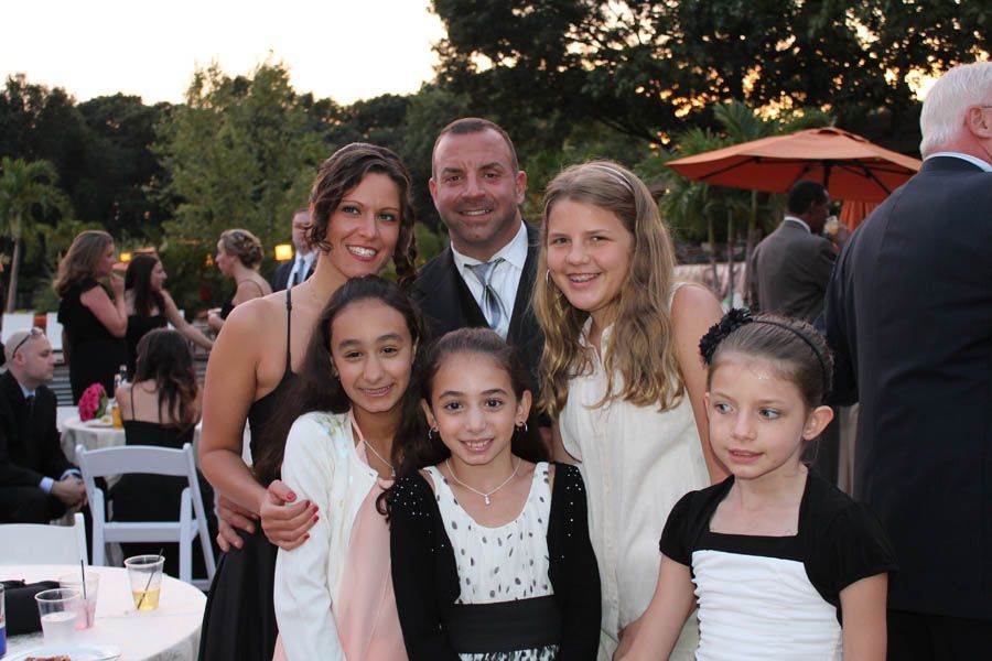 Family posing at an outdoor event; woman and man with four girls smiling.
