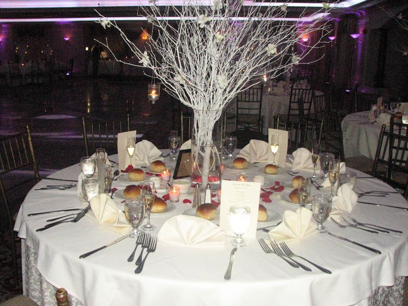 Elegant wedding table setting with white branches, flowers, and candles.
