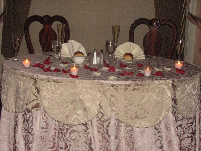 Romantic table setting for two, with candles, rose petals, and bread.