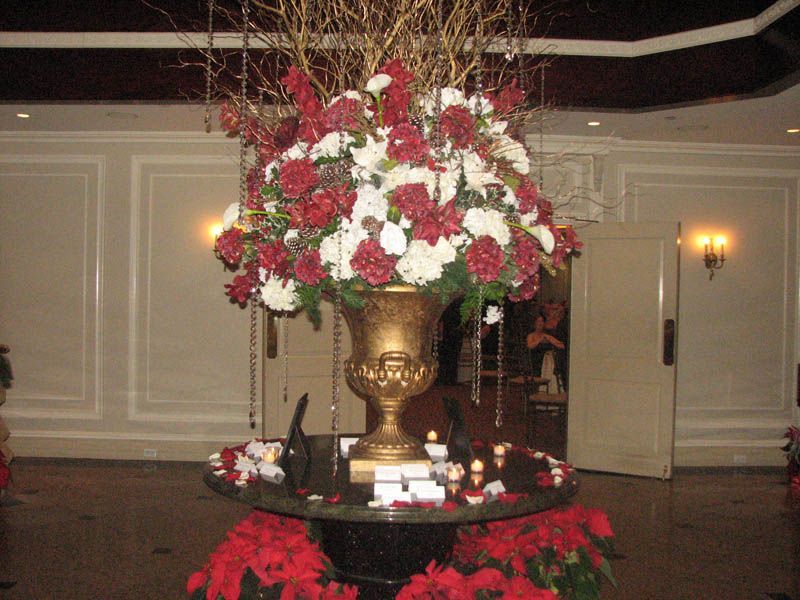 Elegant floral arrangement in gold urn, atop a dark table with poinsettias. Red and white flowers.