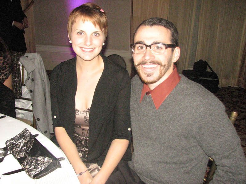 Smiling couple at a table; woman in black cardigan, man in glasses and gray sweater.