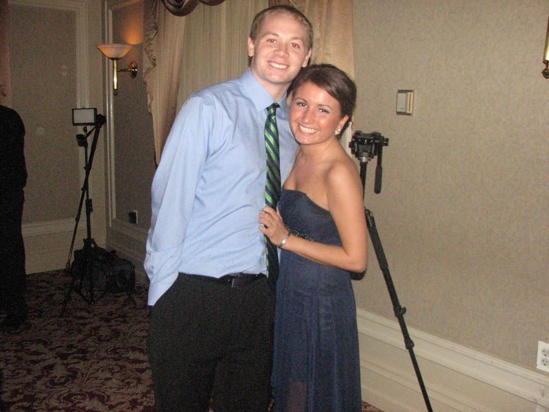 Man in blue shirt and woman in blue dress pose indoors, smiling.