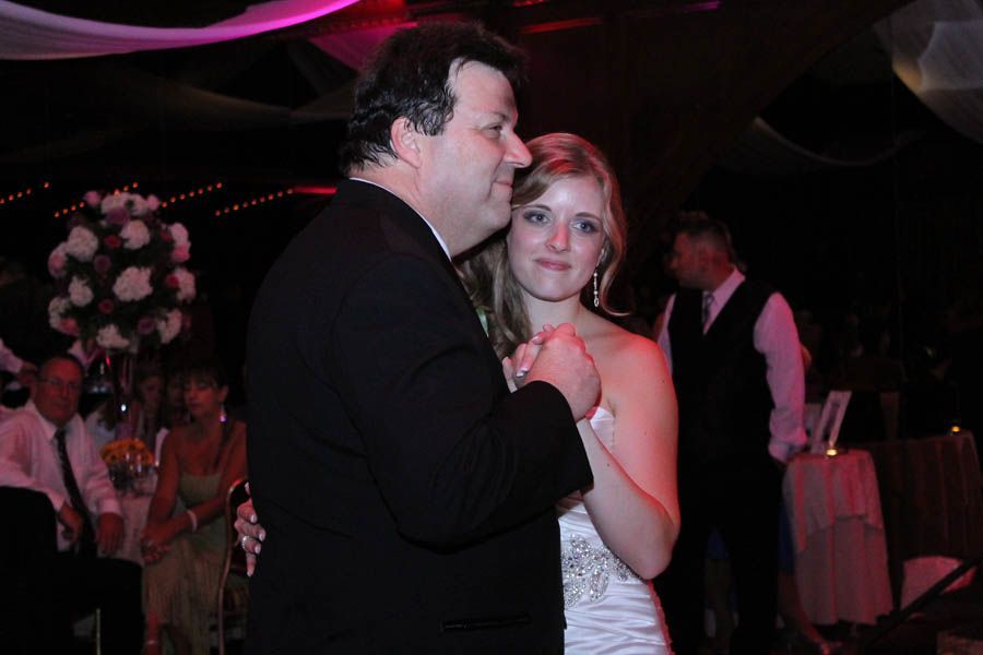 Bride and father dance at a wedding reception. They hold hands; the bride smiles.