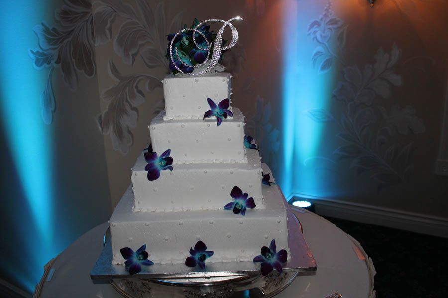 Four-tiered white square wedding cake with blue orchid accents, topped with a 