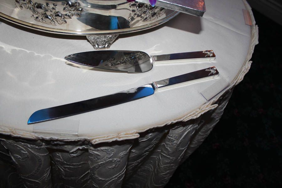 Cake server and knife on a white tablecloth, near a silver cake stand.
