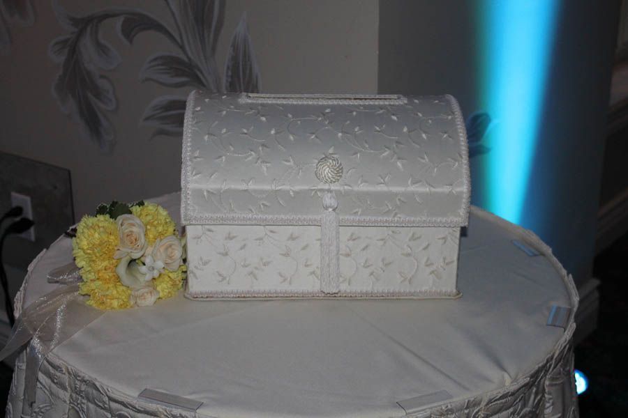 Wedding card box on a table with a bouquet; white and silver, formal setting.