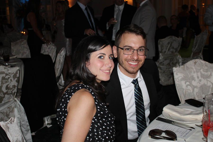Couple smiling at a formal event; woman in polka dots, man in a suit, seated at a table.