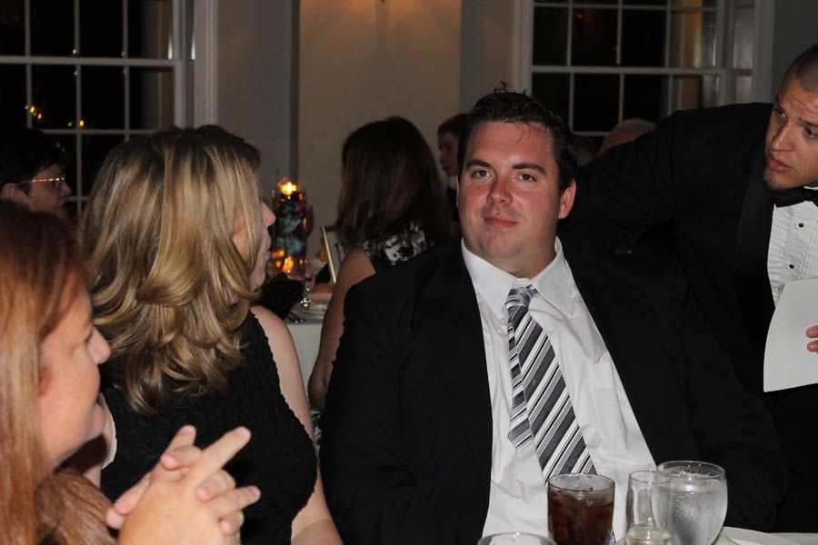 Man in suit at table with others, looking at camera.