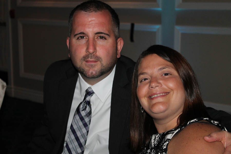 Man in suit and woman with dark hair smile, seated together indoors.