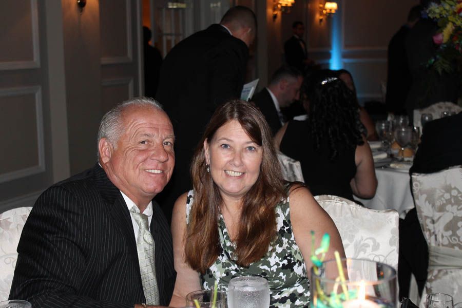Man and woman at a formal table; man in pinstripes smiles, woman in floral print smiles too.