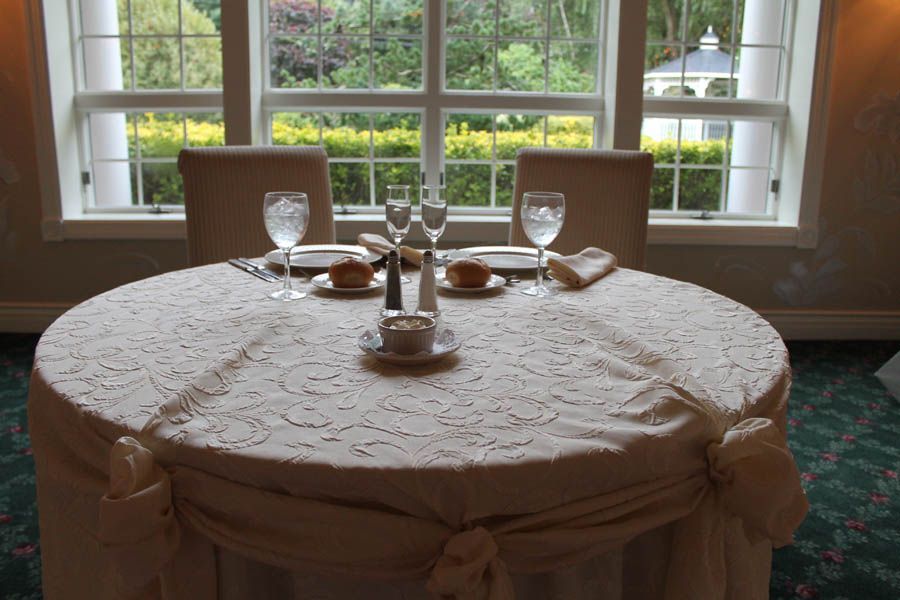 Round table set for two, with window view of gazebo and greenery.