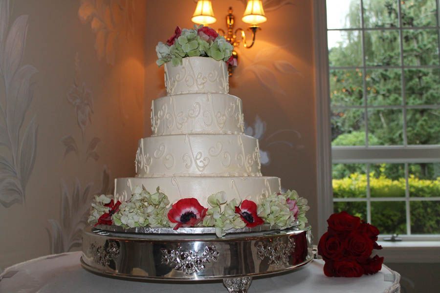 Five-tiered wedding cake on a silver stand, decorated with flowers.