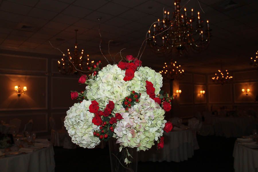 Floral centerpiece with white hydrangeas and red roses in a formal room with chandeliers.