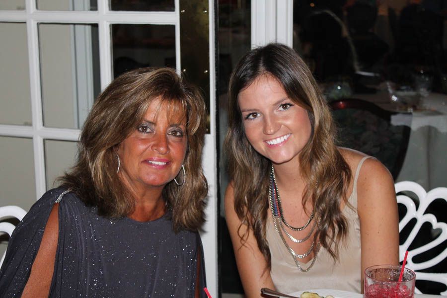 Two women smiling, seated indoors, one wearing a sparkly top and the other a beige top.