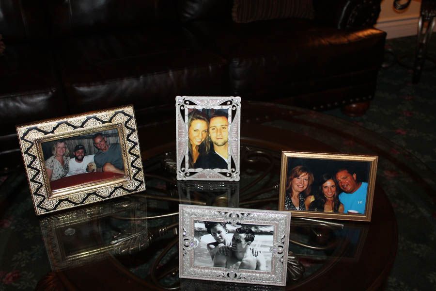 Four framed photos on a glass table in front of a dark leather couch. Photos show groups of people.